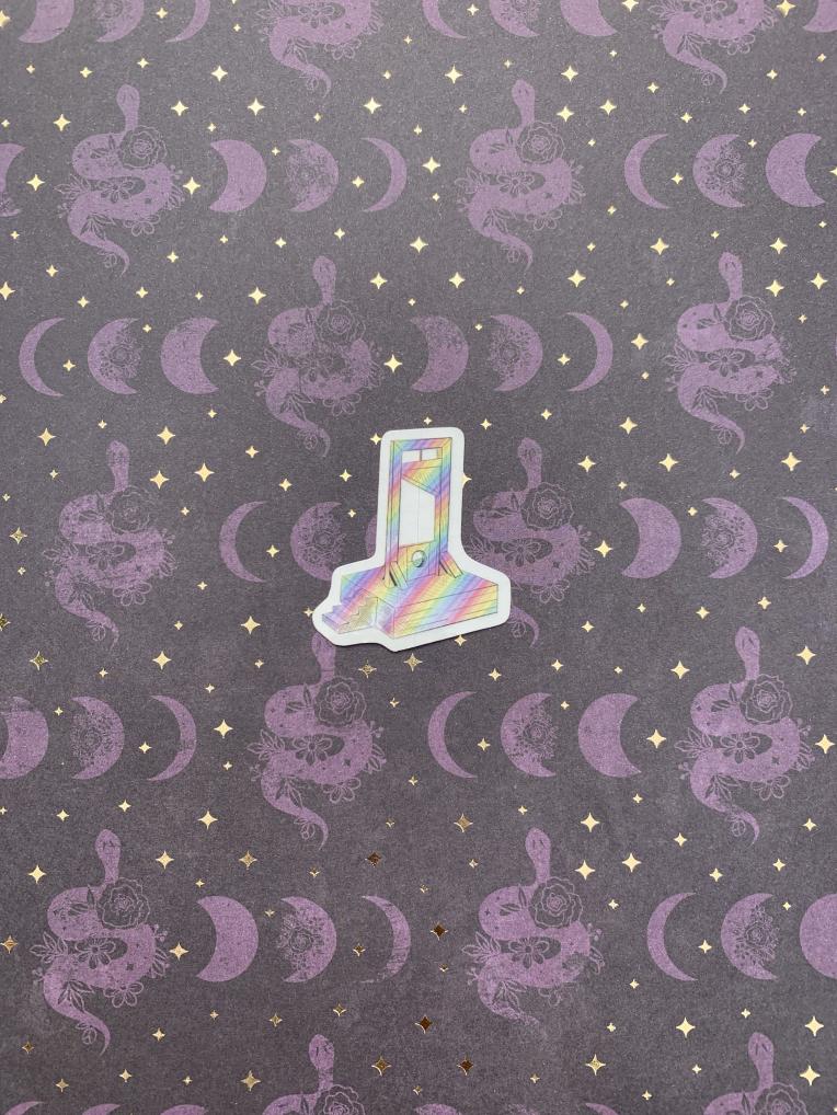 A small rainbow guillotine sticker with a pattern, placed on a background with purple moon and star designs.