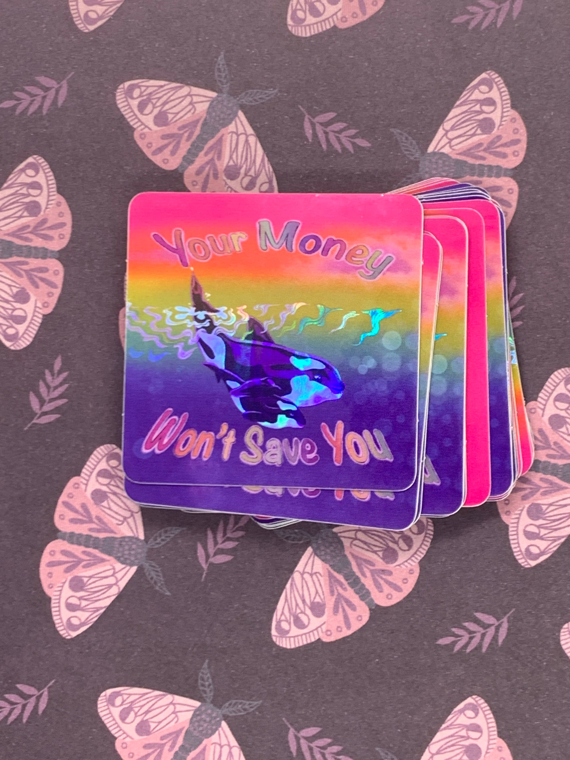 rainbow sticker with big whale and little whale in the water with the words your money won't save you around them the waves in the middle of the sticker are holographic