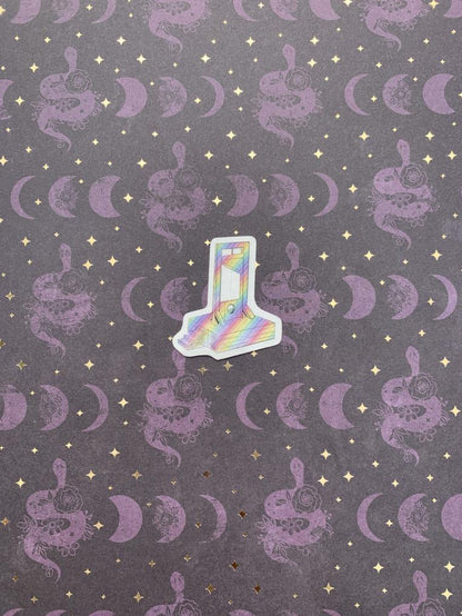 A small rainbow guillotine sticker with a pattern, placed on a background with purple moon and star designs. 